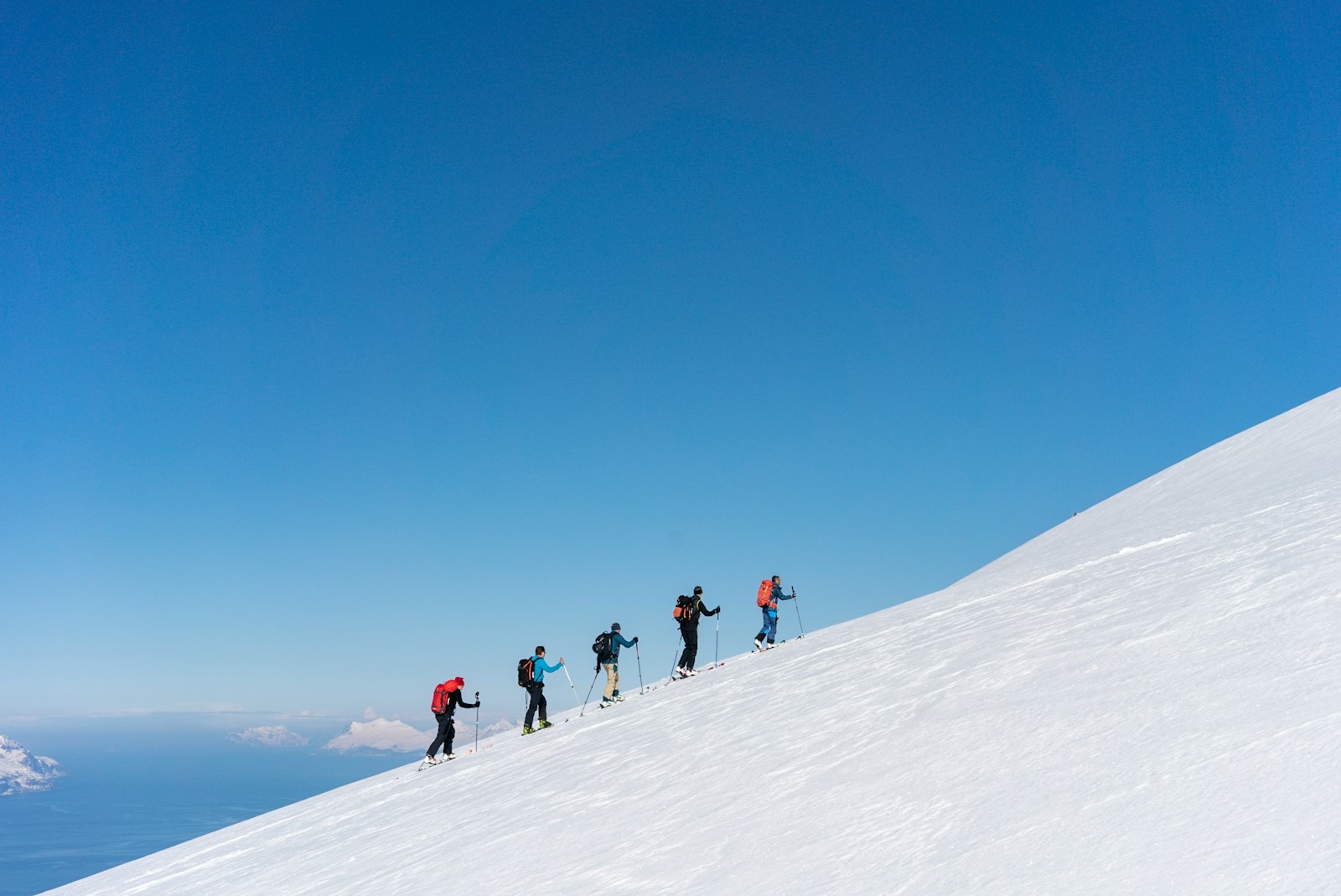 A small guided group skinning a broad ridge with coastal inlets far below