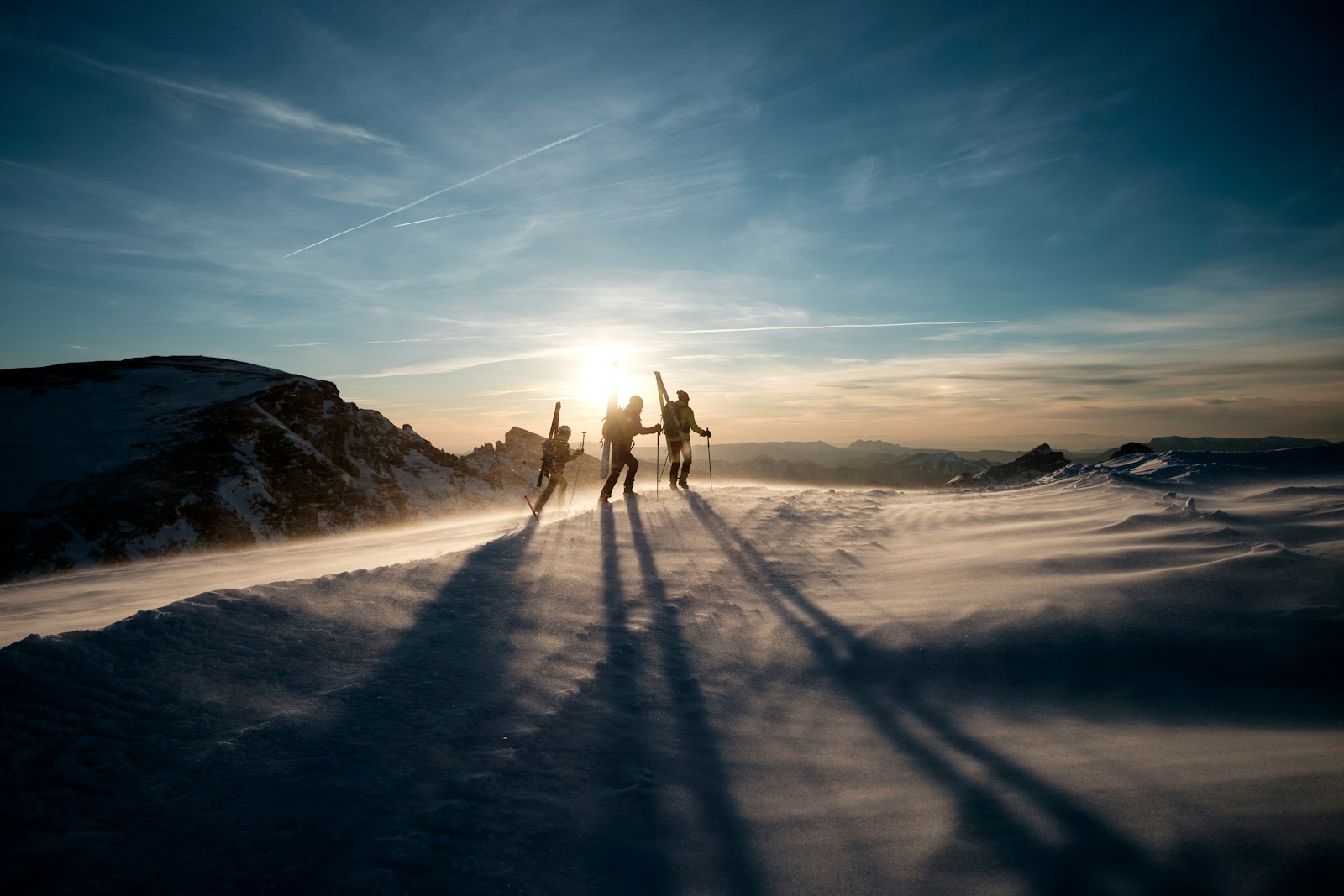 Three ski tourers pausing on a wind-scoured ridge in low light