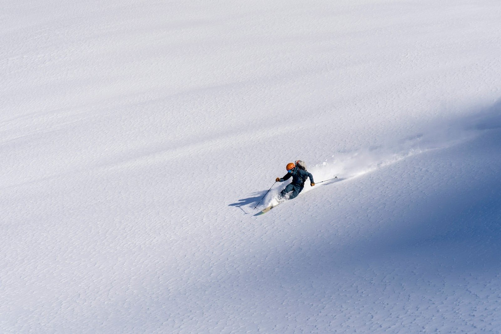 A skier carving a clean turn down an open spring snow slope